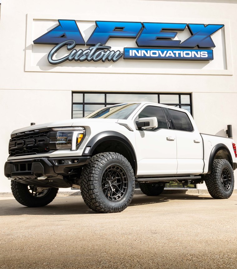 White 2025 Ford F-150 Raptor R on black wheels outside the Apex Custom Innovations showroom