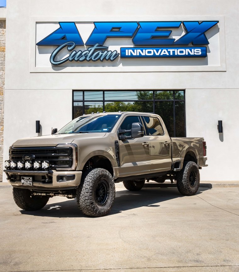 Ford F-350 Super Duty XL in tan with auxiliary lighting outside the Apex Custom Innovations showroom
