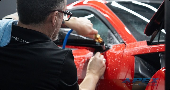 Apex Custom Innovations technician applying paint protection film to a red sports car